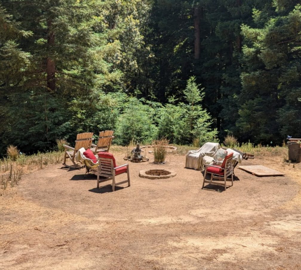 The fire circle on the plateau: wooden chairs around the stone fire pit, forest rising behind